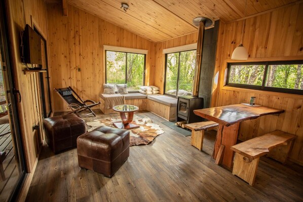 A wooden cabin interior with a sofa, ottoman, dining table, and a fireplace. - La Escondida Pucón (Villarrica)
