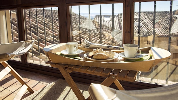 A wooden table with a tray, two cups, and pastries on a balcony with a view of terracotta rooftops. - Lo Raconet de la Plaça (Calaceite)
