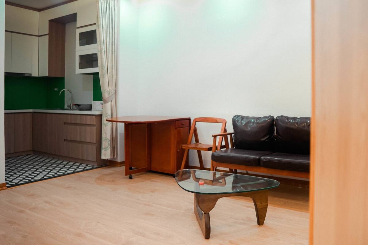 Un espace de vie compact comprenant un coin cuisine, une table basse en verre, un canapé en cuir et une chaise en bois.