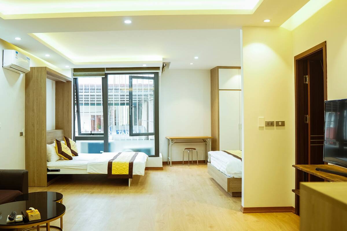 Une chambre d’hôtel moderne équipée d’un lit, d’un bureau, d’une télévision et d’une fenêtre donnant sur des immeubles.