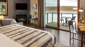 Habitación de hotel con cama, chimenea, televisor, balcón con mesa y sillas, y vista al río.