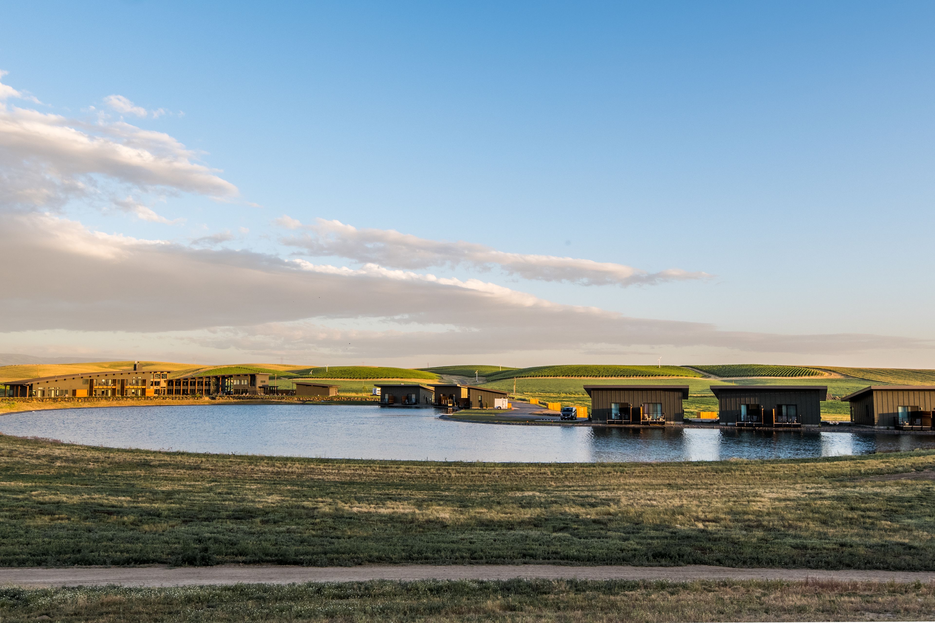 A large building complex with multiple structures, a central water body, and surrounding grassy fields.