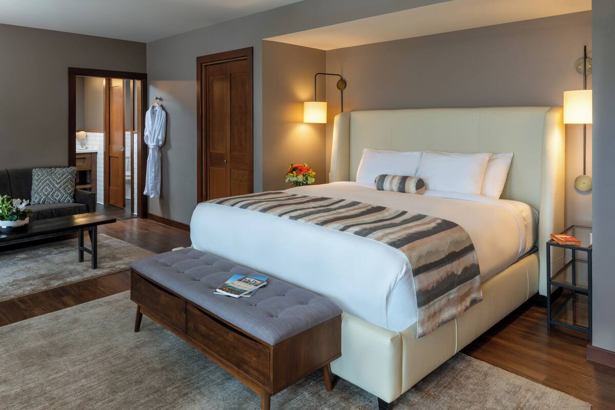 A modern hotel room with a large bed, a bedside table, a bench, and a wardrobe.