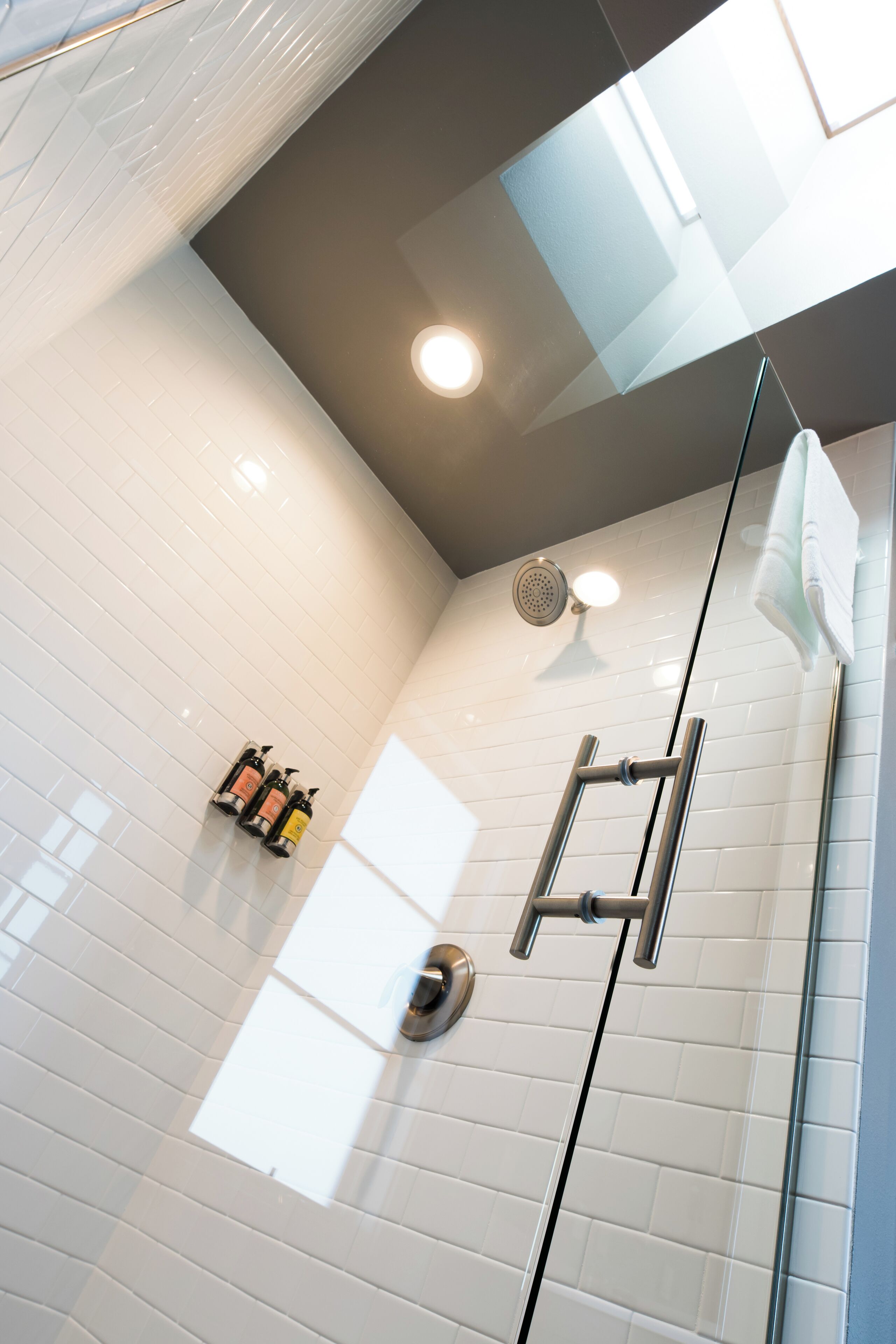 A modern shower area with white tiles, a glass door, and a ceiling light.