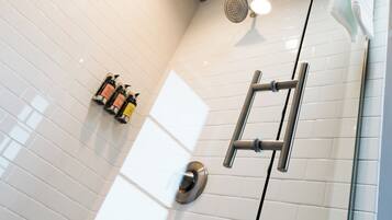 A modern shower area with white tiles, a glass door, and a ceiling light.
