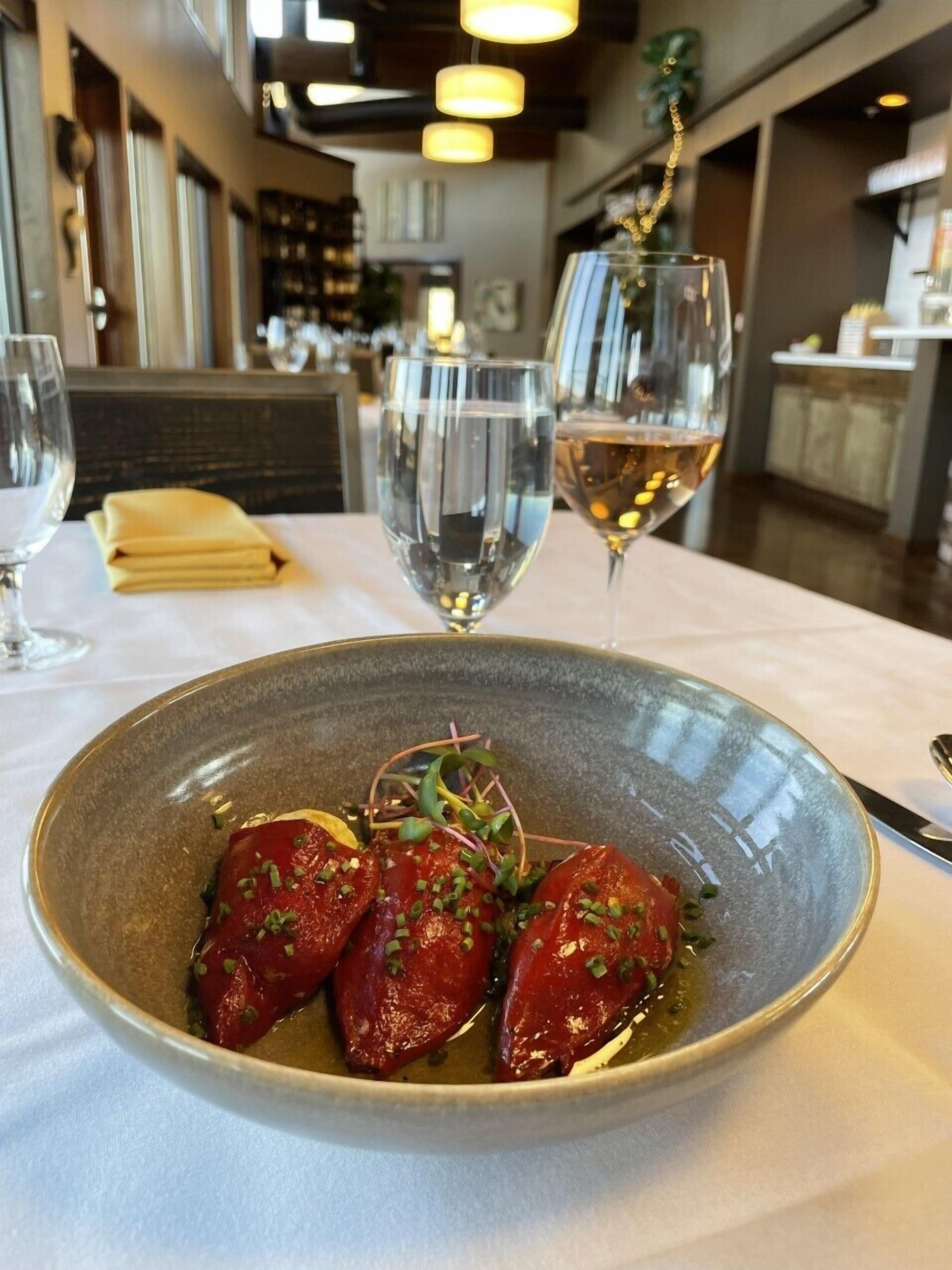 A dining table with a bowl of food and two glasses of wine.