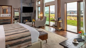 Un dormitorio amplio con una cama grande, una zona de estar con una silla y una mesa, una chimenea y vistas al exterior a través de amplios ventanales.