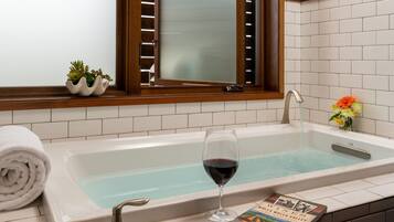 A bathroom with a bathtub, a glass of red wine, a book, and a towel.
