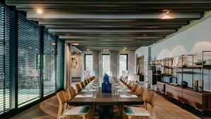 Un salón de conferencias con una larga mesa, sillas de madera y un diseño moderno en el techo.