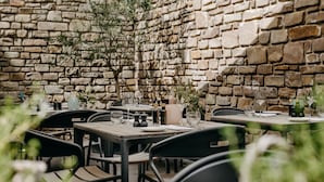Un área de comedor al aire libre con paredes de piedra, mesas dispuestas con copas de vino, platos y cubiertos.