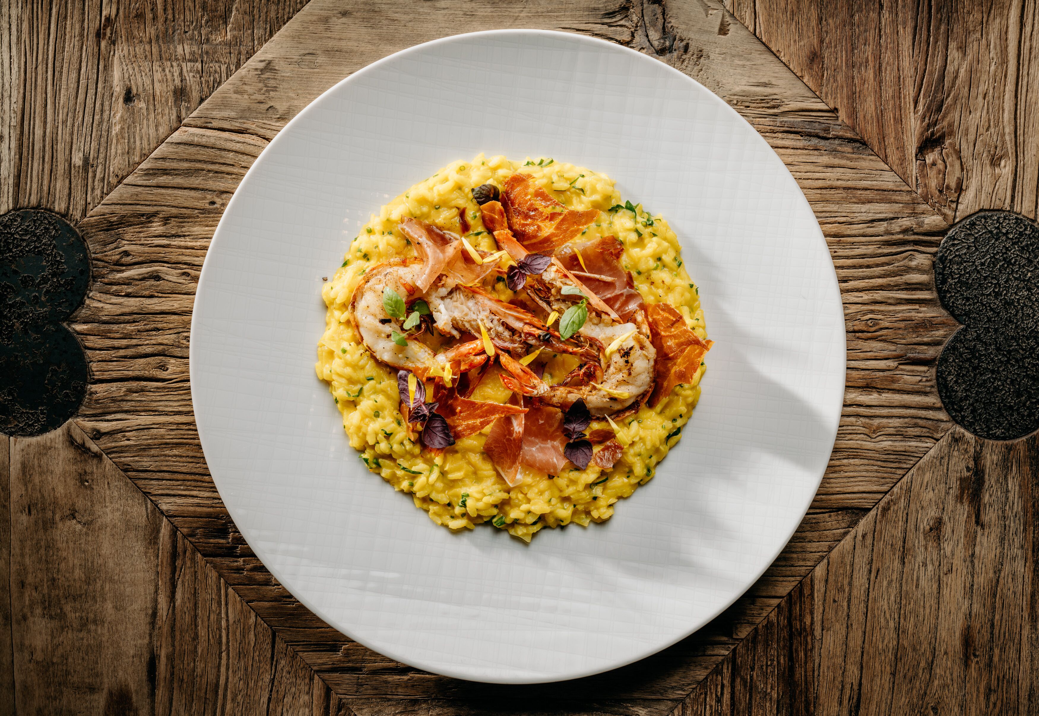 A plate of risotto with shrimp and prosciutto on a wooden table.