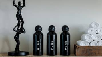 Tres botellas negras etiquetadas como "PURS" sobre una superficie de madera, una estatua negra y una caja de madera con toallas enrolladas.