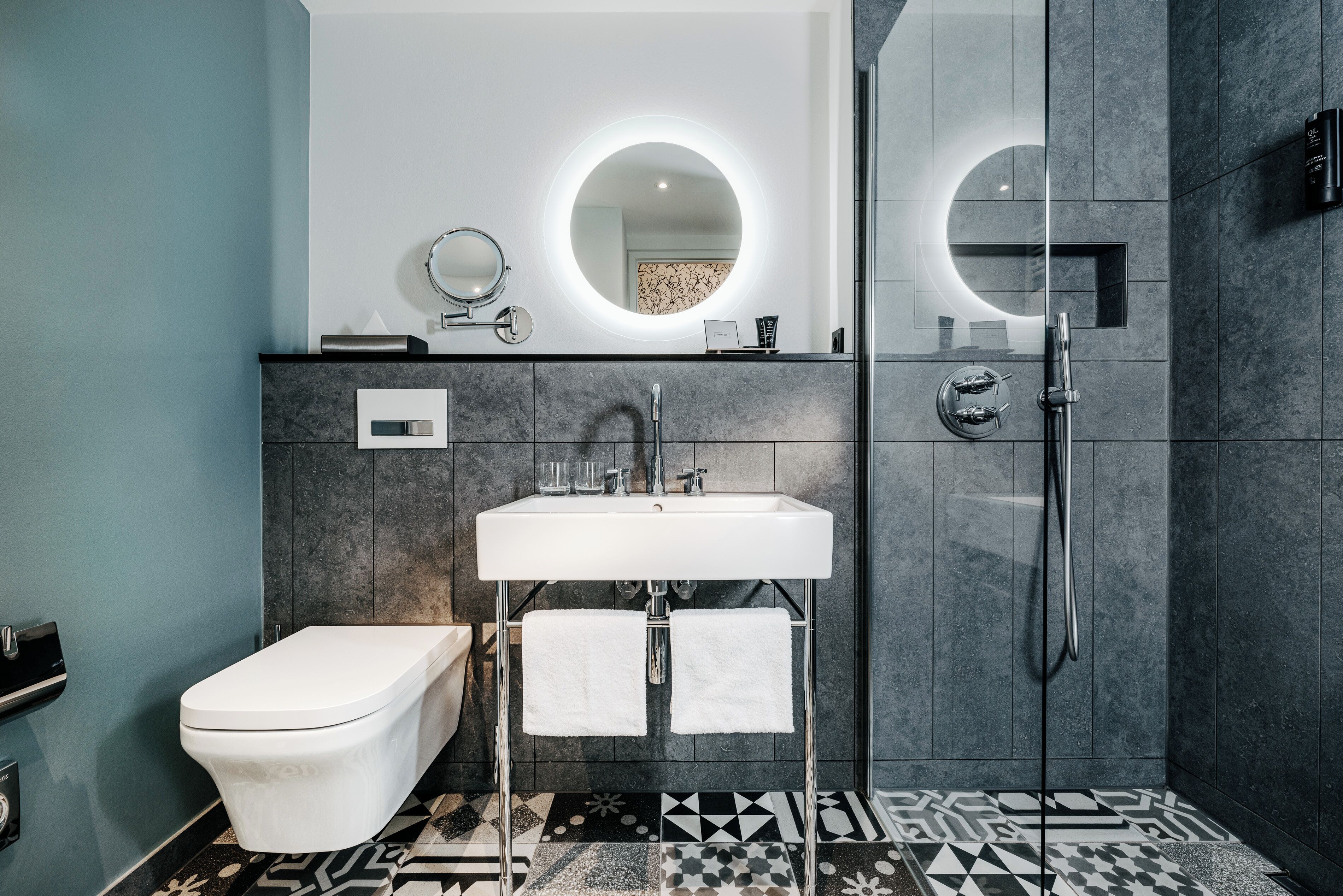 Un baño moderno con inodoro blanco, lavamanos con espejo y zona de ducha.