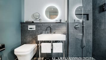 Un baño moderno con inodoro blanco, lavamanos con espejo y zona de ducha.