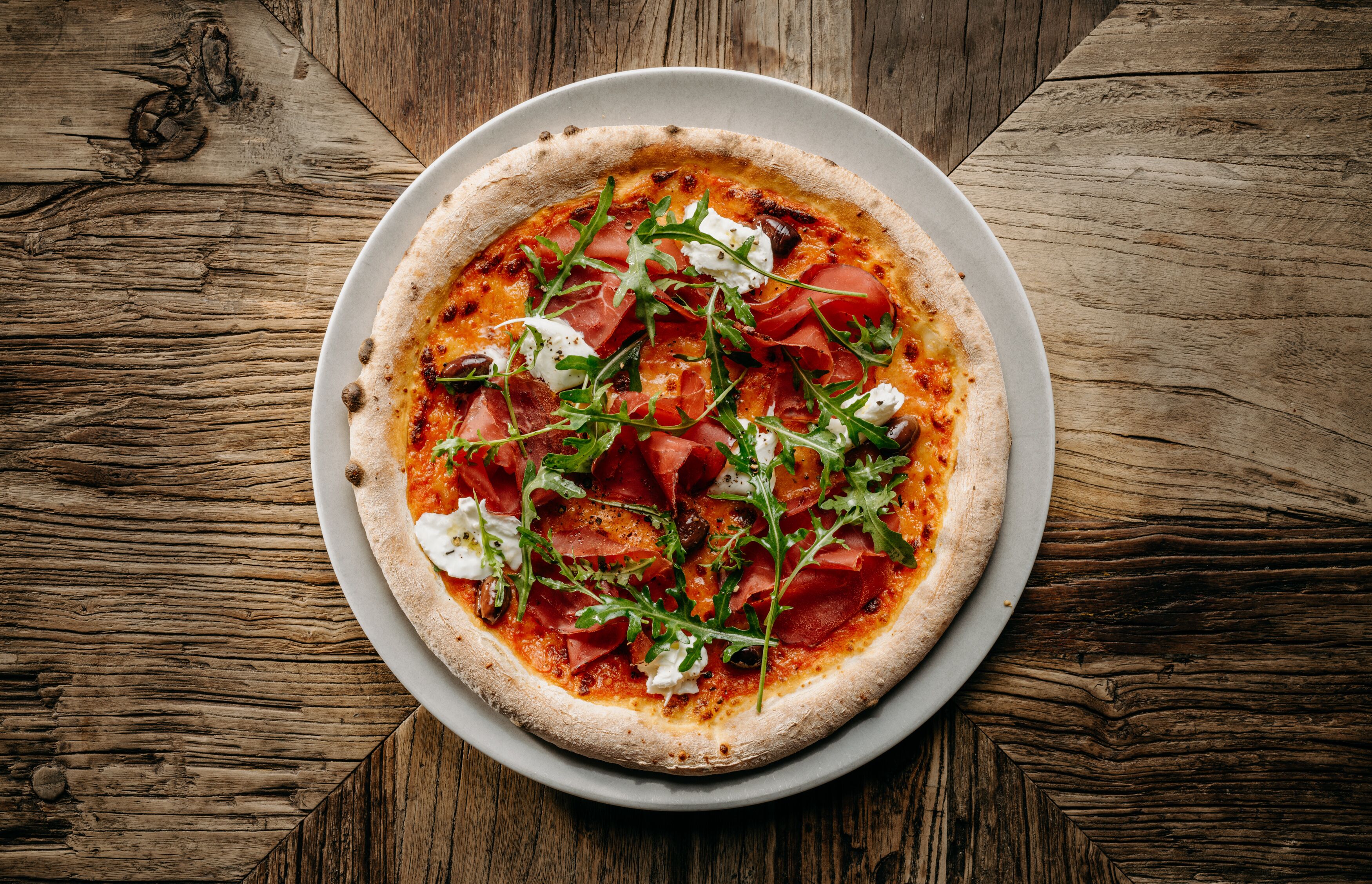 Une pizza sur une assiette blanche, posée sur une table en bois.