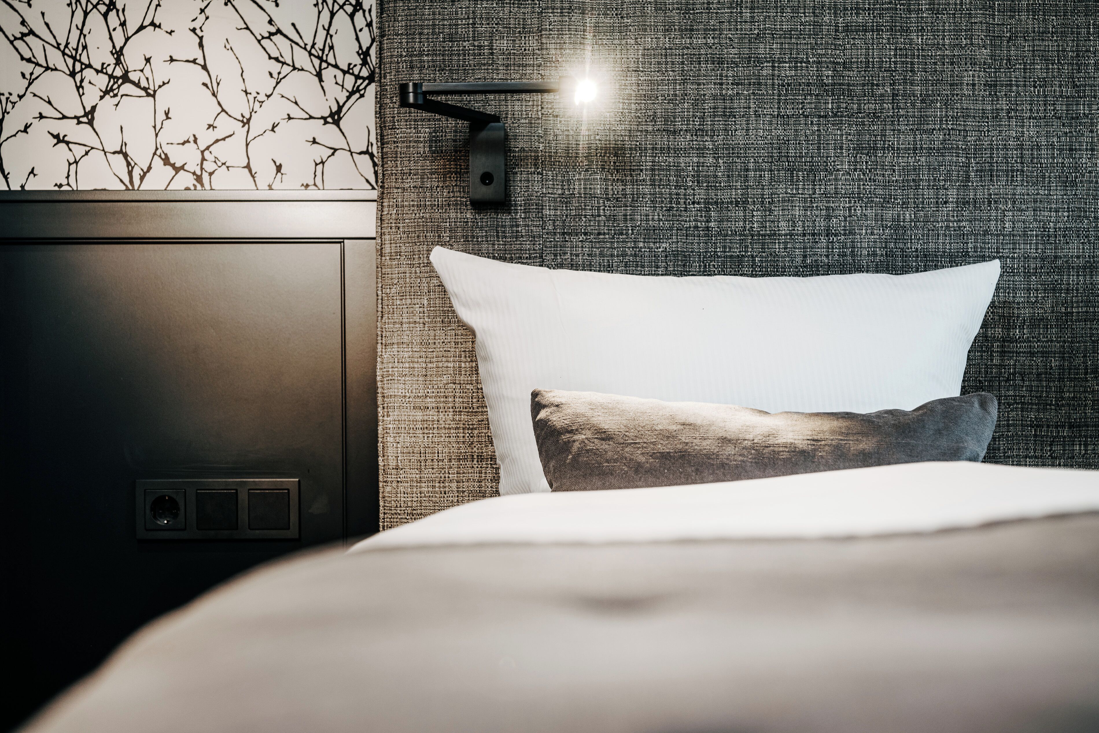 A modern bedroom with a bed, a nightstand, and a wall-mounted lamp.