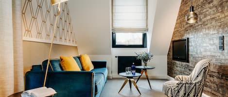 Una sala de estar moderna con un sofá azul, un sillón estampado, una lámpara de pie, una mesita con un florero y vasos, y una chimenea.