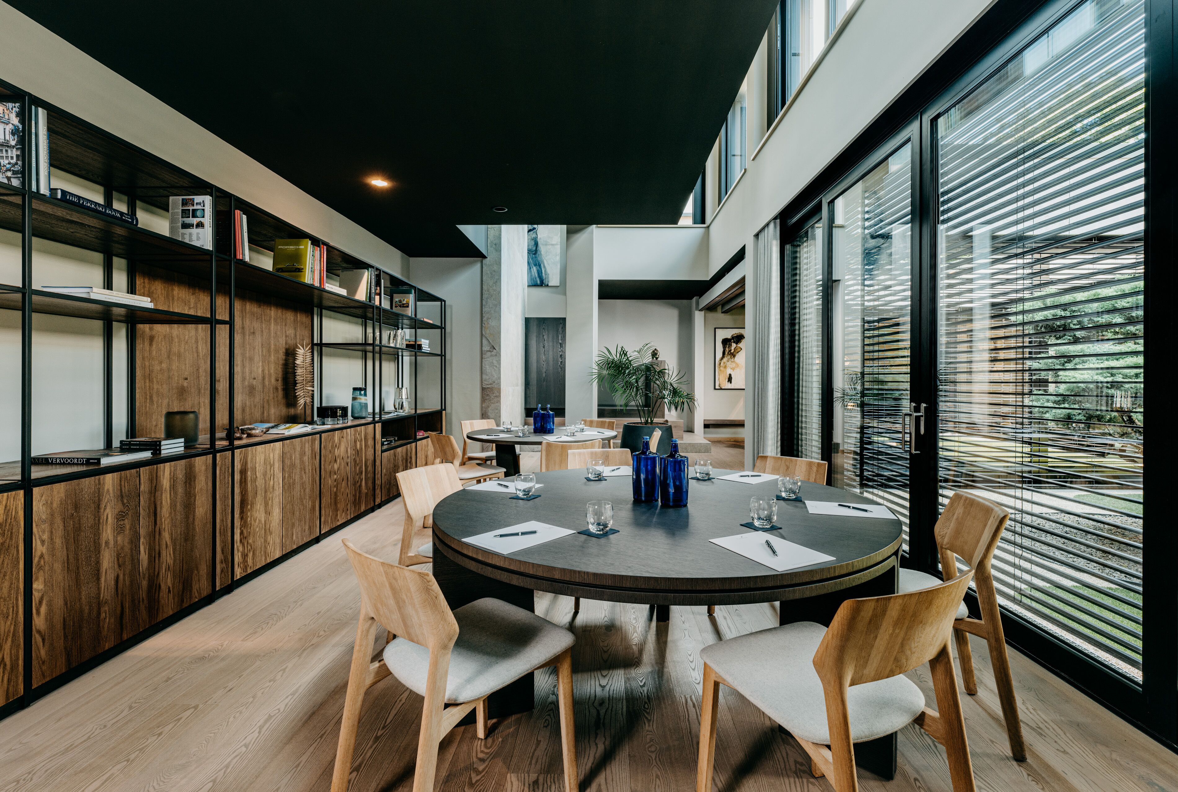 A modern dining area with a round table, wooden chairs, and a bookshelf.