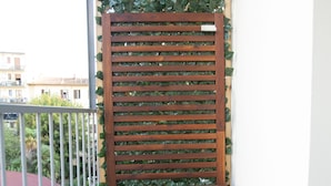 Un balcon avec une table et un banc en bois, une rambarde en métal et un mur couvert de verdure.