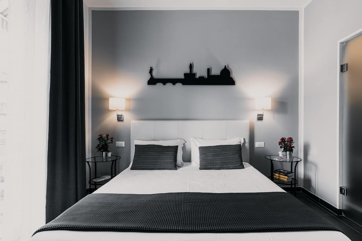Una habitación de hotel moderna con una cama grande, dos mesitas de noche, un cuadro con vistas a la ciudad y una mesita de noche con lámpara.