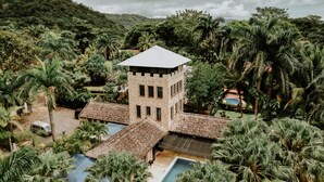 A stone tower with a flat roof, surrounded by lush greenery and a swimming pool. - Castillo Tambor Resort and Restaurant (Cóbano)