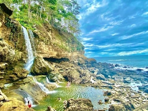 Paisaje natural con cascada, terreno rocoso y un cuerpo de agua.
