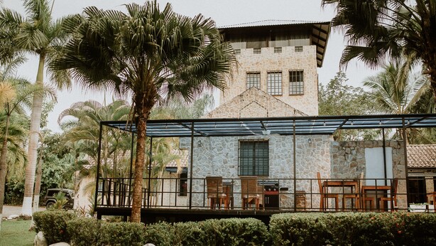 A stone building with a balcony, surrounded by palm trees and rocks. - Castillo Tambor Resort and Restaurant (Cóbano)