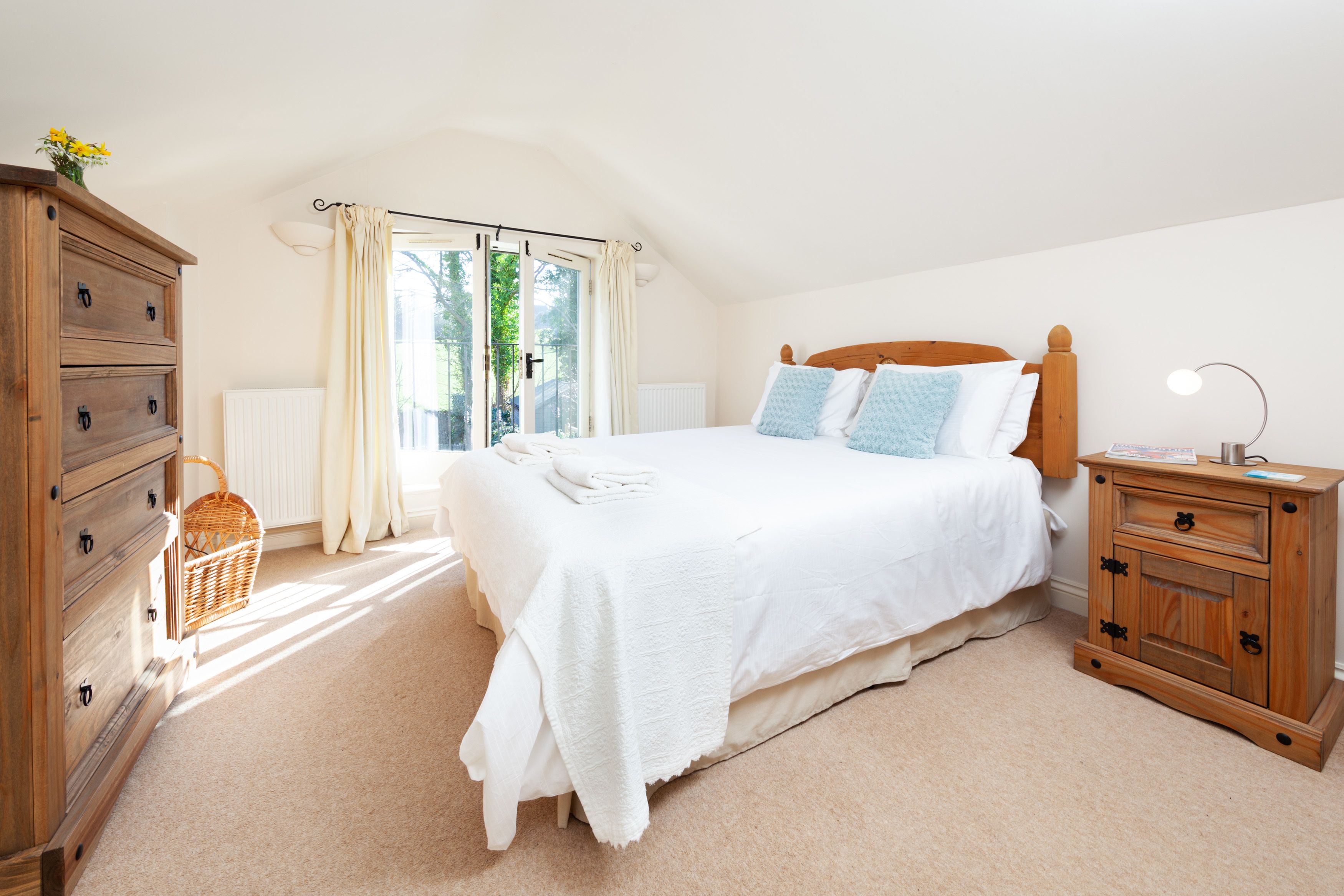 A bedroom with a large bed, wooden dresser, and a window with curtains.