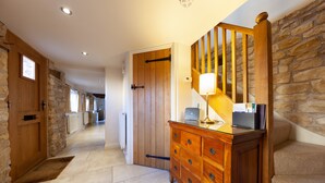A hallway with stone walls, wooden doors, a wooden dresser with drawers, and a lamp. - Camside, Chipping Campden - Taswell Retreats (Chipping Campden)