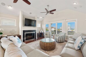 A modern living room with a fireplace, comfortable seating, a flat-screen TV, and a ceiling fan.