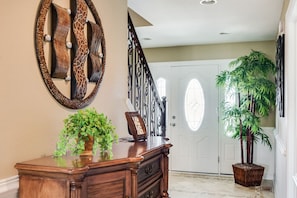 A foyer with a wooden desk, a wall clock, a potted plant, and a staircase.