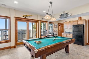 A pool table in a room with wooden cabinets, a refrigerator, and a sign that says "Welcome".