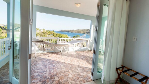 A balcony with stone flooring, a white table, and a hammock. - Sea Turtle Studio – Upscale Waterview Retreat, Stunning Sunrises & Full Kitchen! (Culebra)