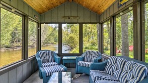 A covered outdoor seating area with striped furniture, large windows, and a view of a river.
