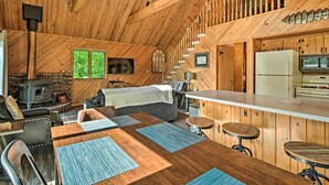 A cozy cabin interior with a wooden interior, a fireplace, a dining area, and a kitchen with a refrigerator and stove.