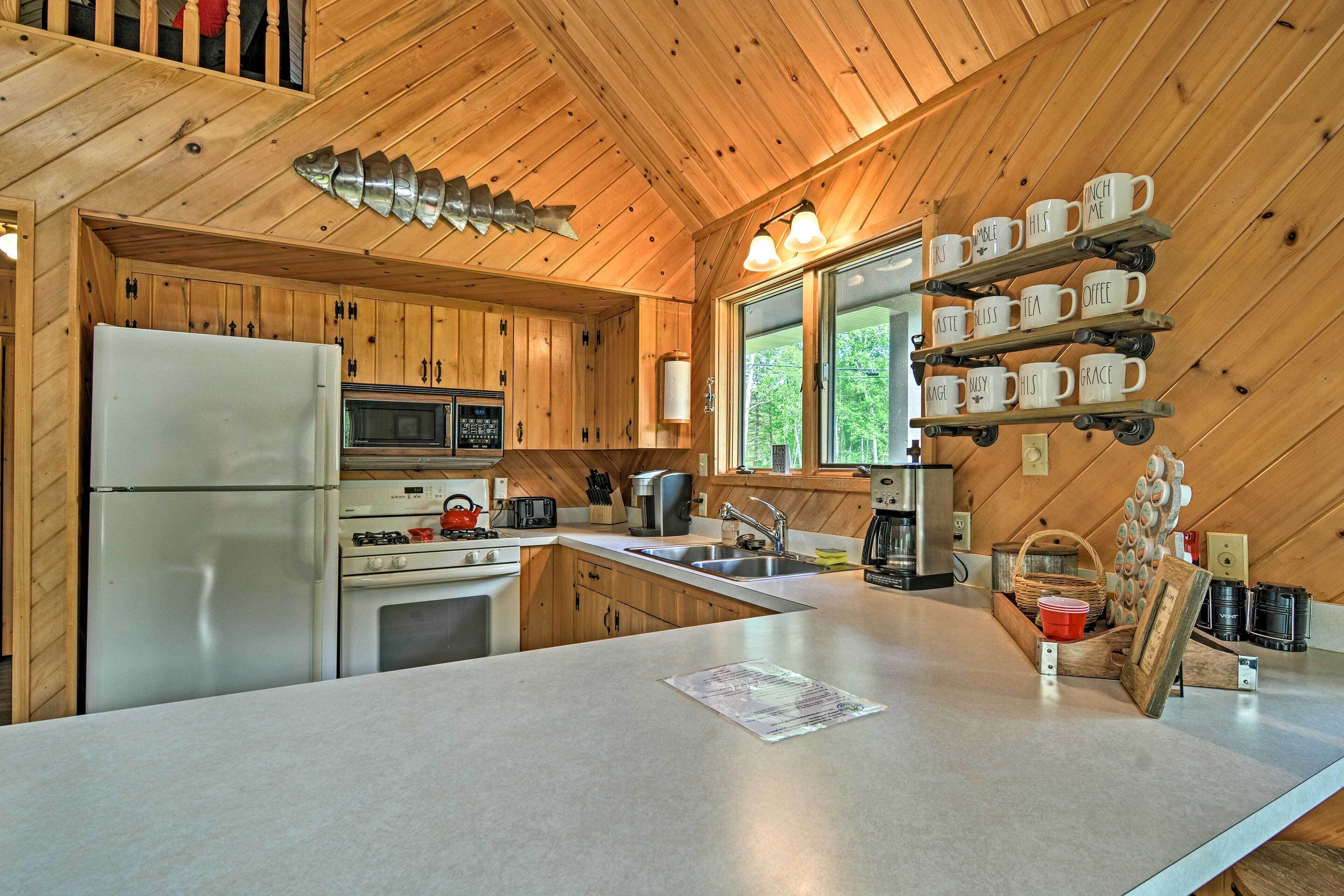 Une cuisine rustique aménagée dans une cabane en bois, équipée d’un réfrigérateur, d’un four à micro-ondes, d’une cuisinière et d’un coin café.