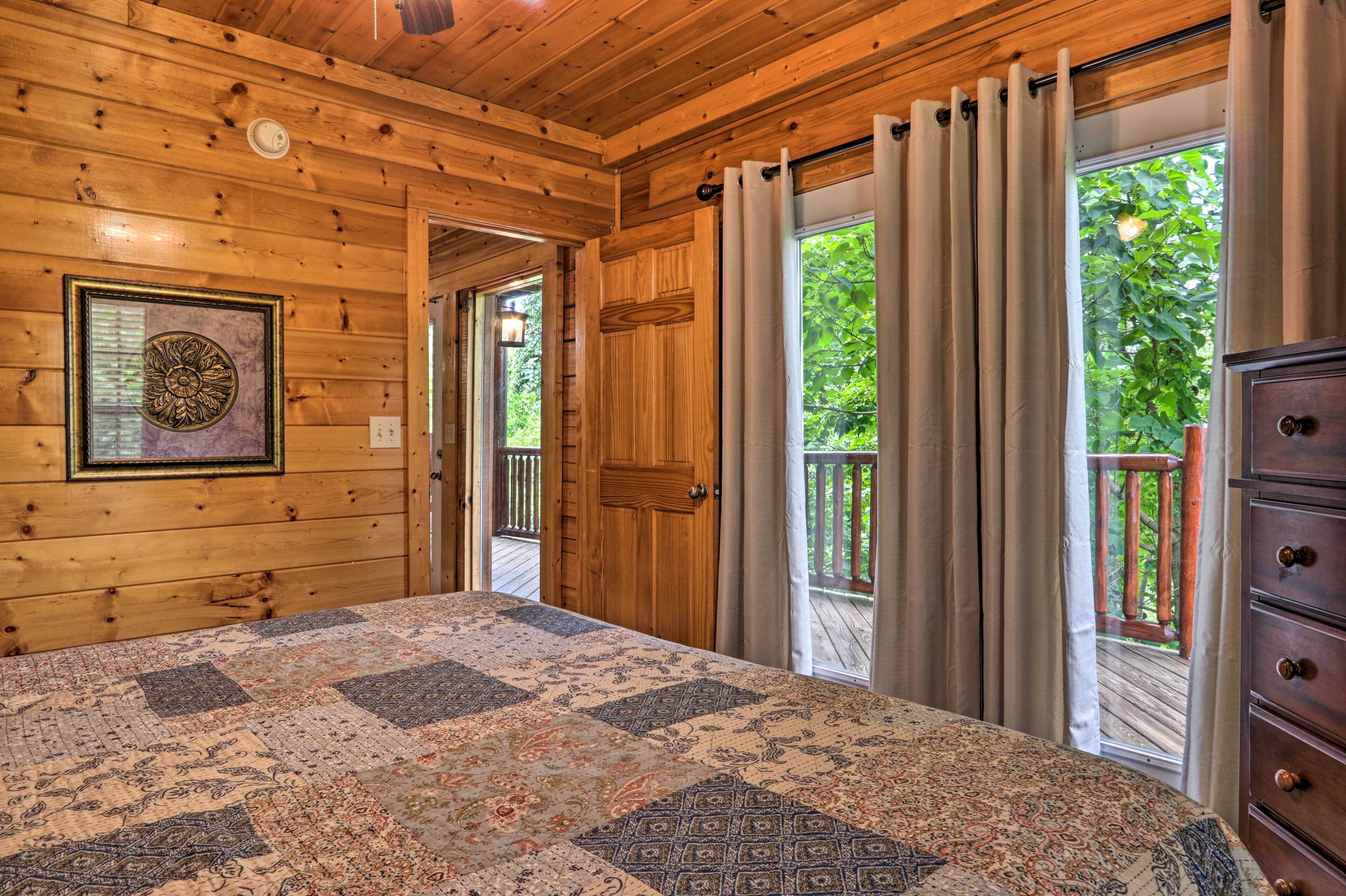 Un dormitori de cabana de fusta amb un llit gran, un quadre amb marc a la paret i vista a l'exterior a través d'una porta corredissa.