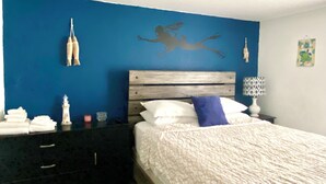 A bedroom with a blue wall, a wooden headboard, a white bed with a patterned blanket, a nightstand with a lamp, and decorative items including a lighthouse and a silhouette of a person. - Escape to Nature - 2 miles from Ichetucknee park  (Fort White)