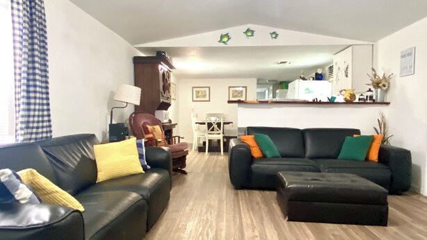 A living room with a black leather sofa, a dining table with chairs, a wooden floor, and a kitchen area in the background. - Escape to Nature - 2 miles from Ichetucknee park  (Fort White)