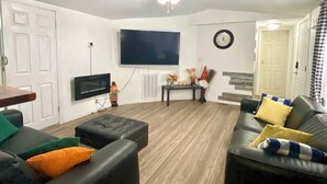 A living room with a flat-screen TV, a ceiling fan, a clock, and a sofa with cushions. - Escape to Nature - 2 miles from Ichetucknee park  (Fort White)