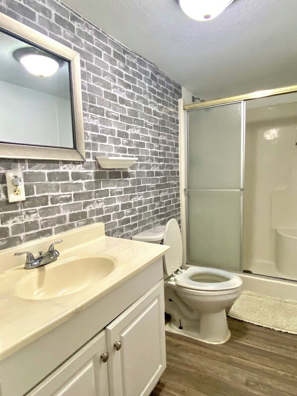 A bathroom with a brick wall, a white sink, a toilet, and a glass shower enclosure.
