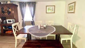 A dining area with a dark wooden table, white chairs, a white tablecloth, and a decorative border. There is a microwave on a shelf, a cabinet with glass doors, and two framed pictures on the wall. - Escape to Nature - 2 miles from Ichetucknee park  (Fort White)