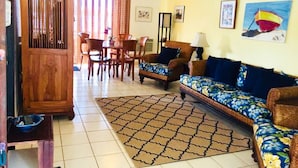 Una sala de estar con un sofá, sillas, un aparador de madera y un tapete estampado.