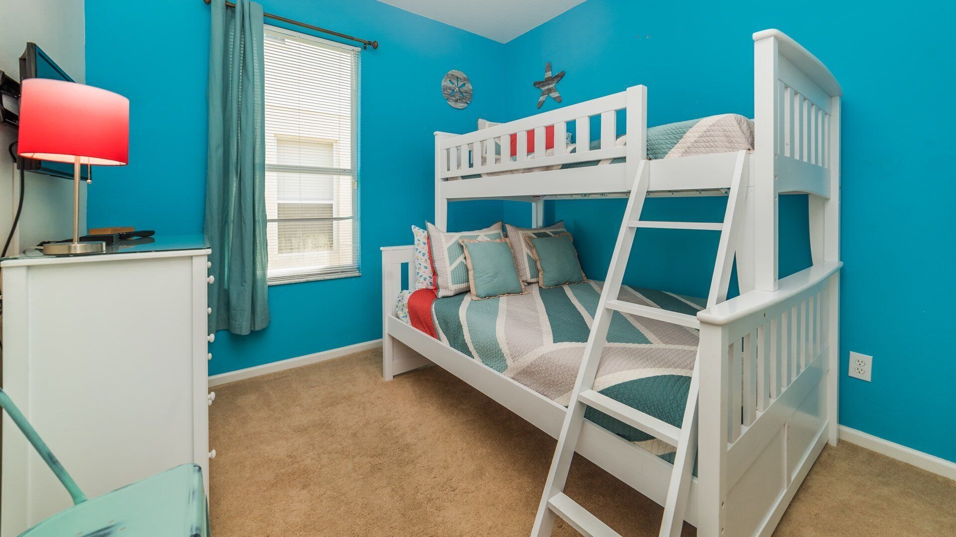 A room with a bunk bed, a desk with a lamp, a window with blinds, and a wall clock.