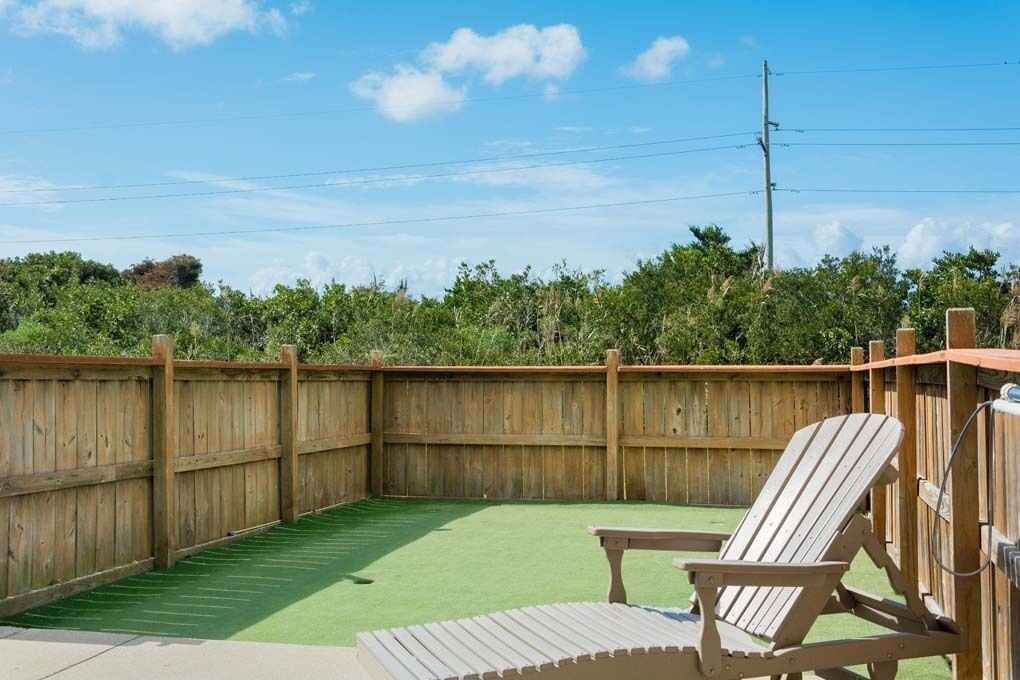 Un patio trasero con terraza de madera, césped artificial verde y valla de madera.