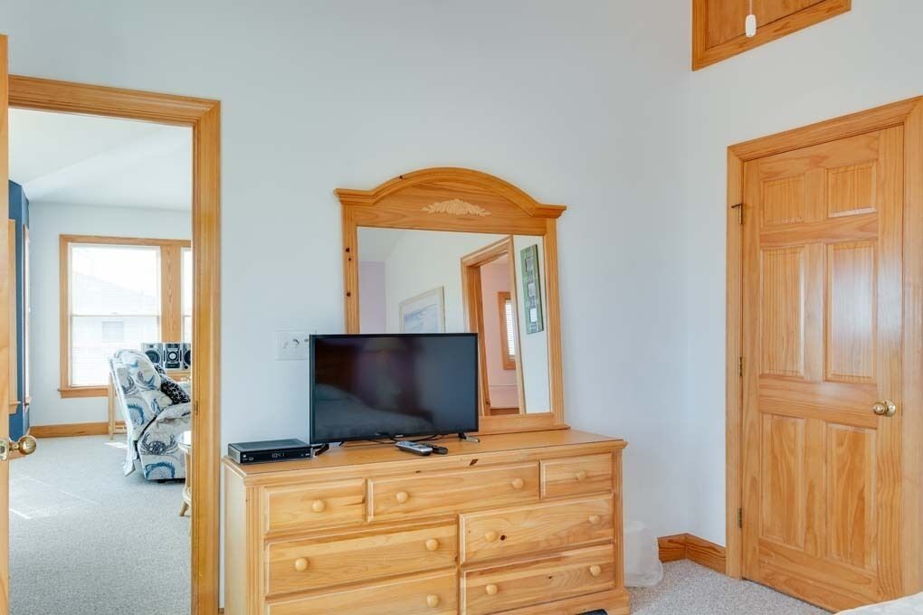 Una habitación con un aparador de madera, un televisor de pantalla plana, un espejo sobre el aparador y una puerta a la derecha.