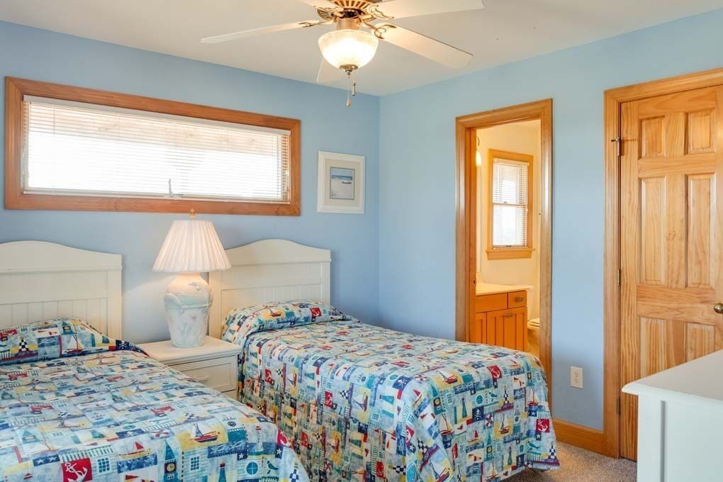 Un dormitorio con dos camas, ventilador de techo, ventana con persianas y puerta de madera.