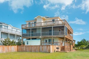 A multi-story residential building with a balcony on the upper floor, a garage, and a fenced yard.