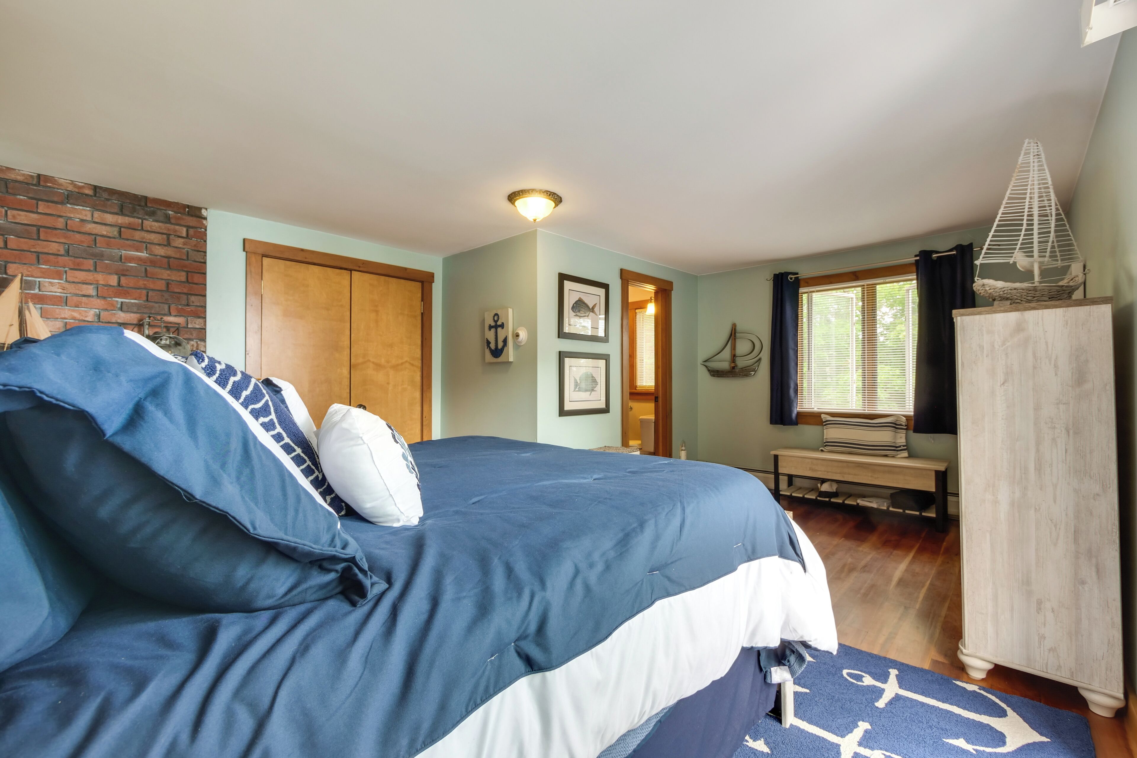 Een slaapkamer met een groot bed, een houten garderobe, een bankje en een raam met gordijnen.
