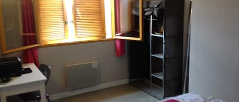 A room with a bed, a desk, a chair, a radiator, and a wardrobe.